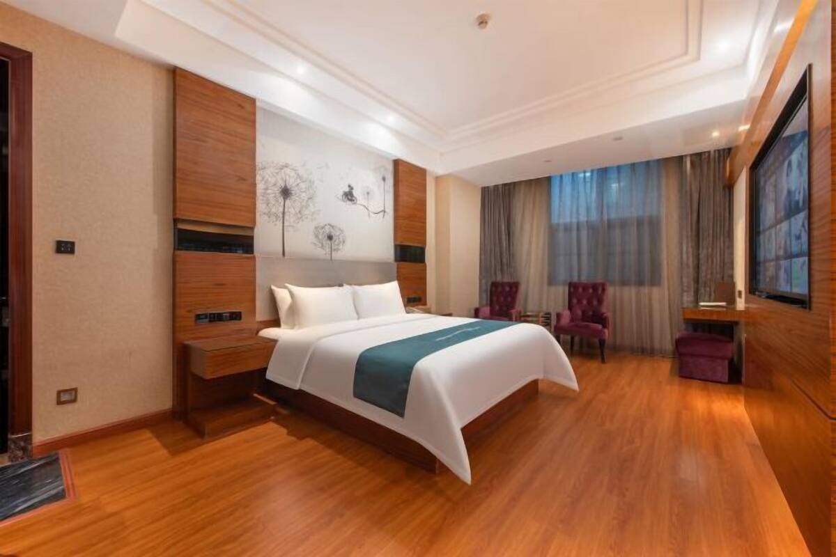 A modern hotel room with a large bed, wooden flooring, a desk, and a chair.