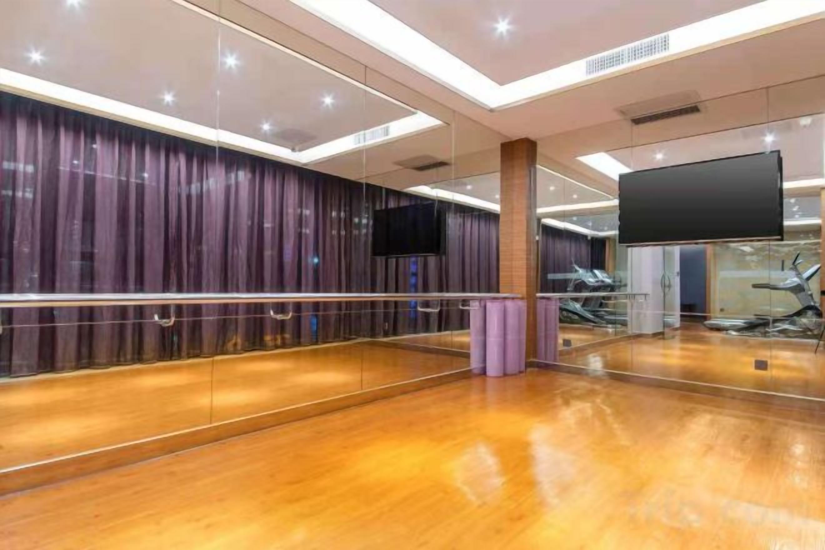A spacious dance studio with a wooden floor, a large mirror, and a television screen.