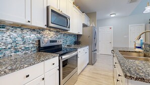 A modern kitchen with white cabinets, a stainless steel refrigerator, a built-in microwave, and a granite countertop. - Shared Pool, Pet Friendly, Golf Cart Access (Port Aransas)