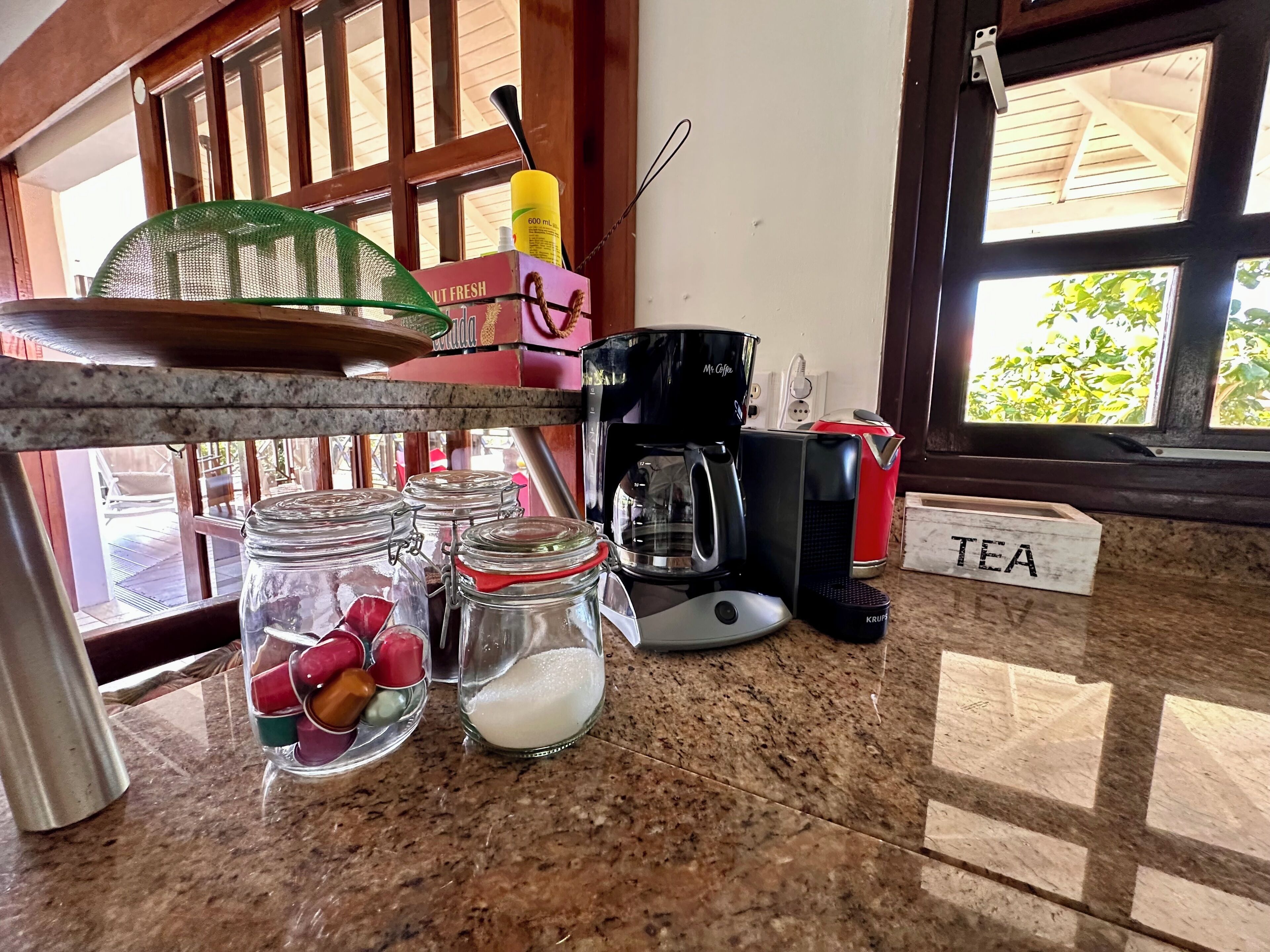 A kitchen counter with a coffee maker, a tea sign, and jars of sugar and spices.