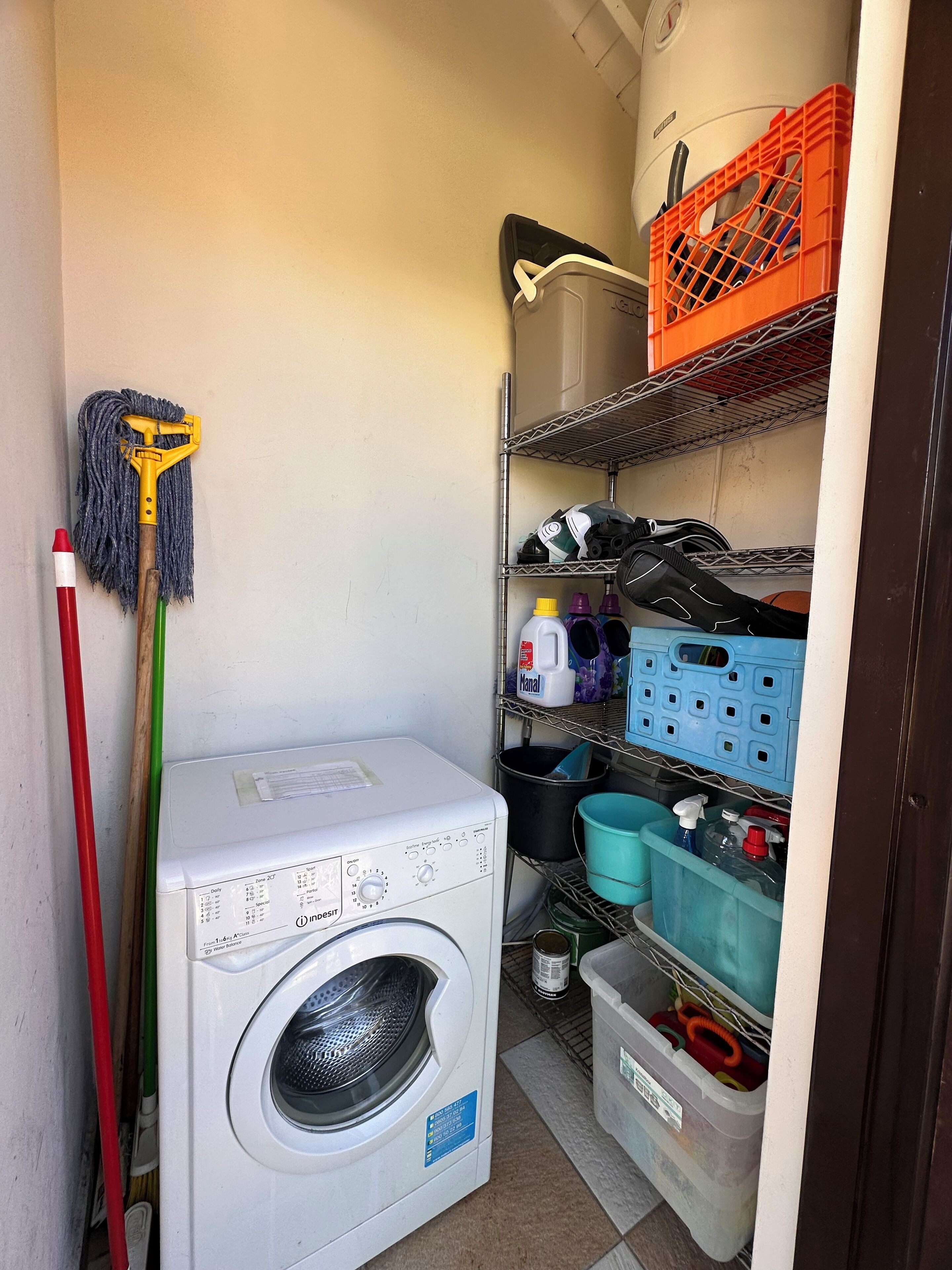 Une buanderie équipée d’un lave-linge, d’étagères contenant des produits de nettoyage et d’une serpillière.