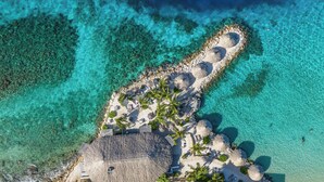 Ett flygbildsbild av ett strandresort med kristallklart turkosfärgat vatten, en sandstrand, palmer och byggnader med halmtak.