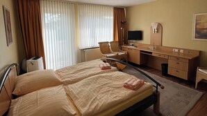 Ein Hotelzimmer mit zwei Betten, einem Schreibtisch, einem Stuhl, einem Fernseher und einem Fenster mit Vorhängen.