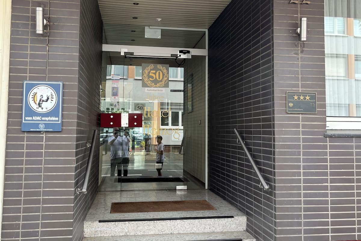 Entrada de hotel con toldo rojo, un letrero que indica 50 años de servicio y el número '22' en la pared.