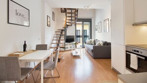 A modern living space with a dining area, a staircase, a sofa, and a kitchen. - Happy Travel Churruca 25 (Málaga)