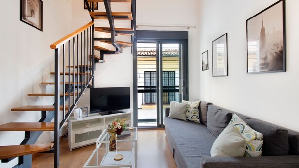 A modern living room with a staircase, a sofa, a coffee table, and a television. - Happy Travel Churruca 25 (Málaga)