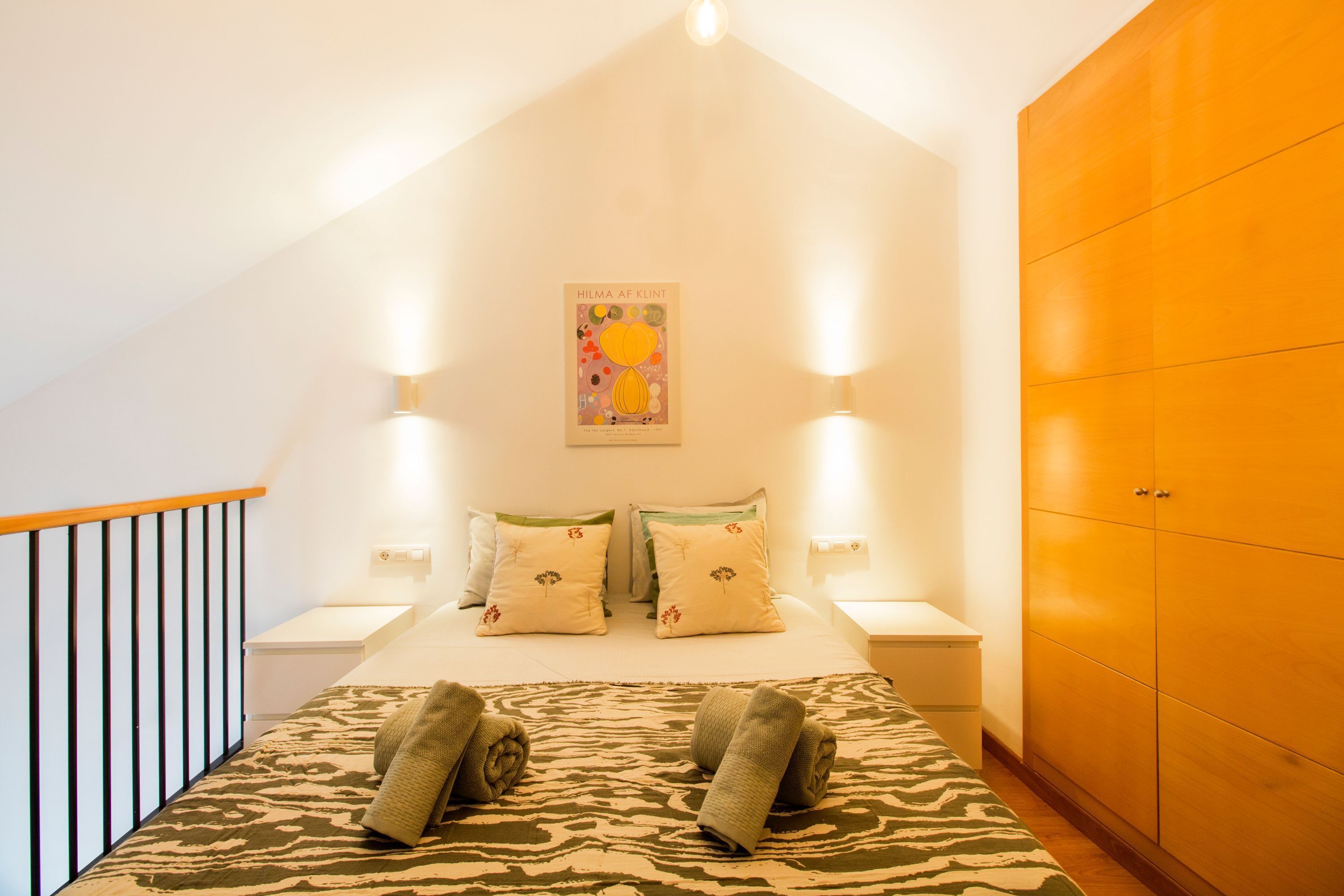 Une chambre à coucher avec un lit, deux tables de chevet, une armoire en bois et une affiche accrochée au mur.