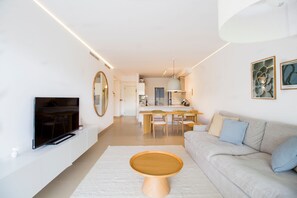 Una sala de estar moderna con un televisor de pantalla plana, una mesa de centro de madera, un sofá y un comedor con una mesa y sillas.