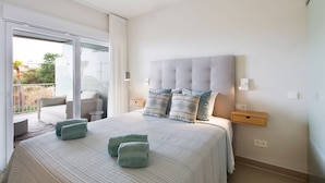 Une chambre avec un grand lit, un balcon avec une chaise et une table de chevet avec une lampe.