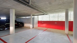 Un parking avec des piliers en béton, un mur rouge et une voiture noire garée dans une place.