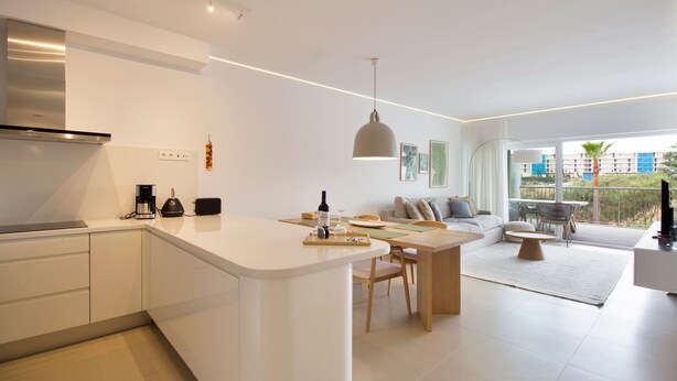 Une cuisine moderne dotée d’un îlot central, un coin repas avec une table et des chaises, et un salon avec un canapé et un téléviseur.