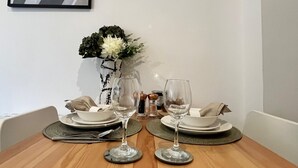 Une table à manger dressée avec des assiettes, des couverts et deux verres à vin, agrémentée d’un vase de fleurs et d’un objet décoratif.