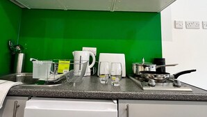 Une cuisine avec des armoires blanches, un pare-feu vert et divers ustensiles de cuisine, comme une bouilloire, des verres et une poêle.