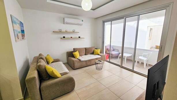 A living room with two sofas, a coffee table, and a TV. There is a sliding glass door leading to a balcony with outdoor furniture. - Seaside Comfort Residence (Larnaca)