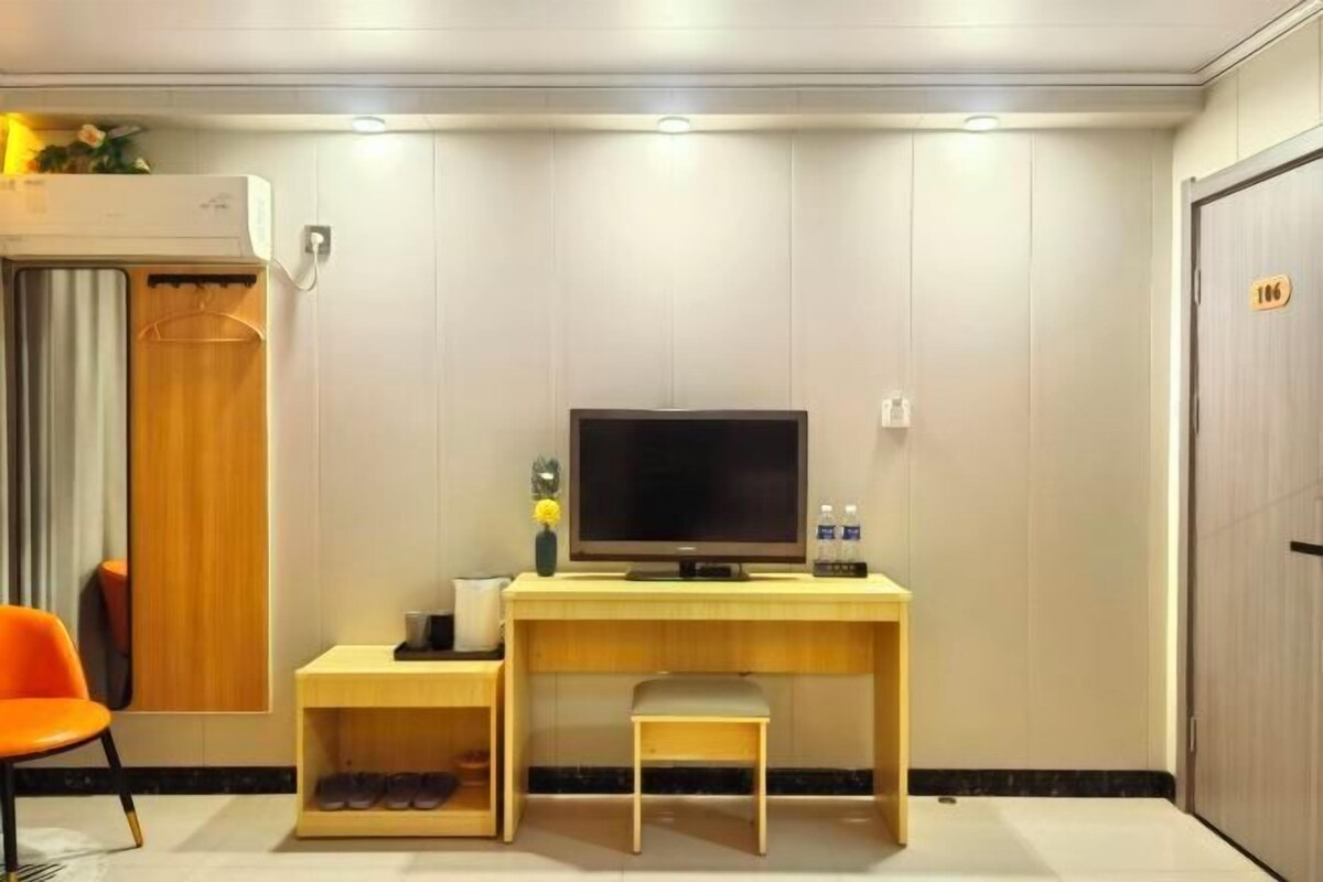 A hotel room with a wooden desk, a television, a chair, a shoe rack, and a wardrobe.