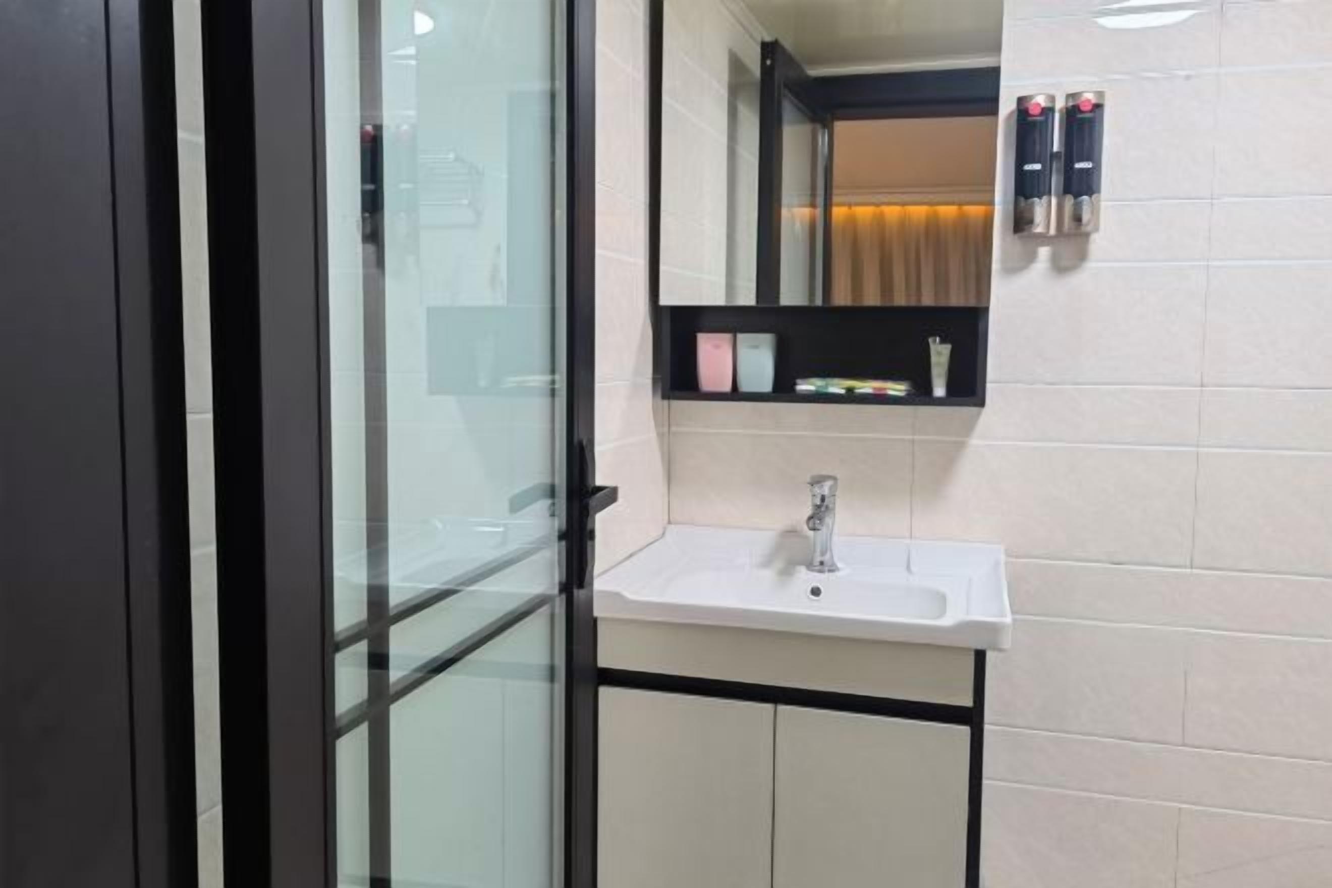 Ein modernes Badezimmer mit Glastrennwand, Waschbecken in Weiß, Spiegel und Ablage mit Toilettenartikeln.