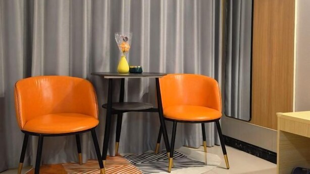 Una habitación con dos sillones naranjas, una mesita con un florero y un armario de madera.