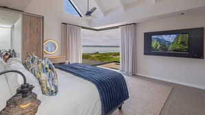 A modern bedroom with a large bed, a ceiling fan, a TV, and a view of the outdoors. - The Shark Bay Private Villas (Langebaan)