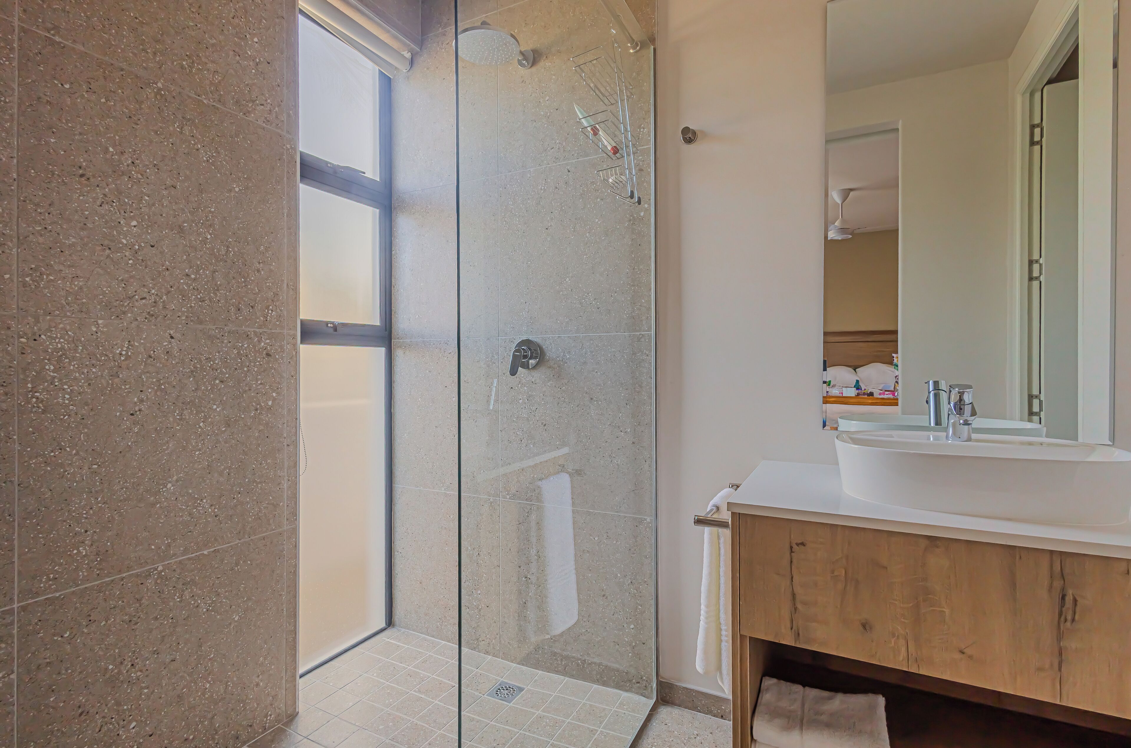 Un baño moderno con ducha envuelta en vidrio, un lavabo blanco y un mueble de tocador de madera.