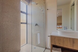 Un baño moderno con ducha envuelta en vidrio, un lavabo blanco y un mueble de tocador de madera.