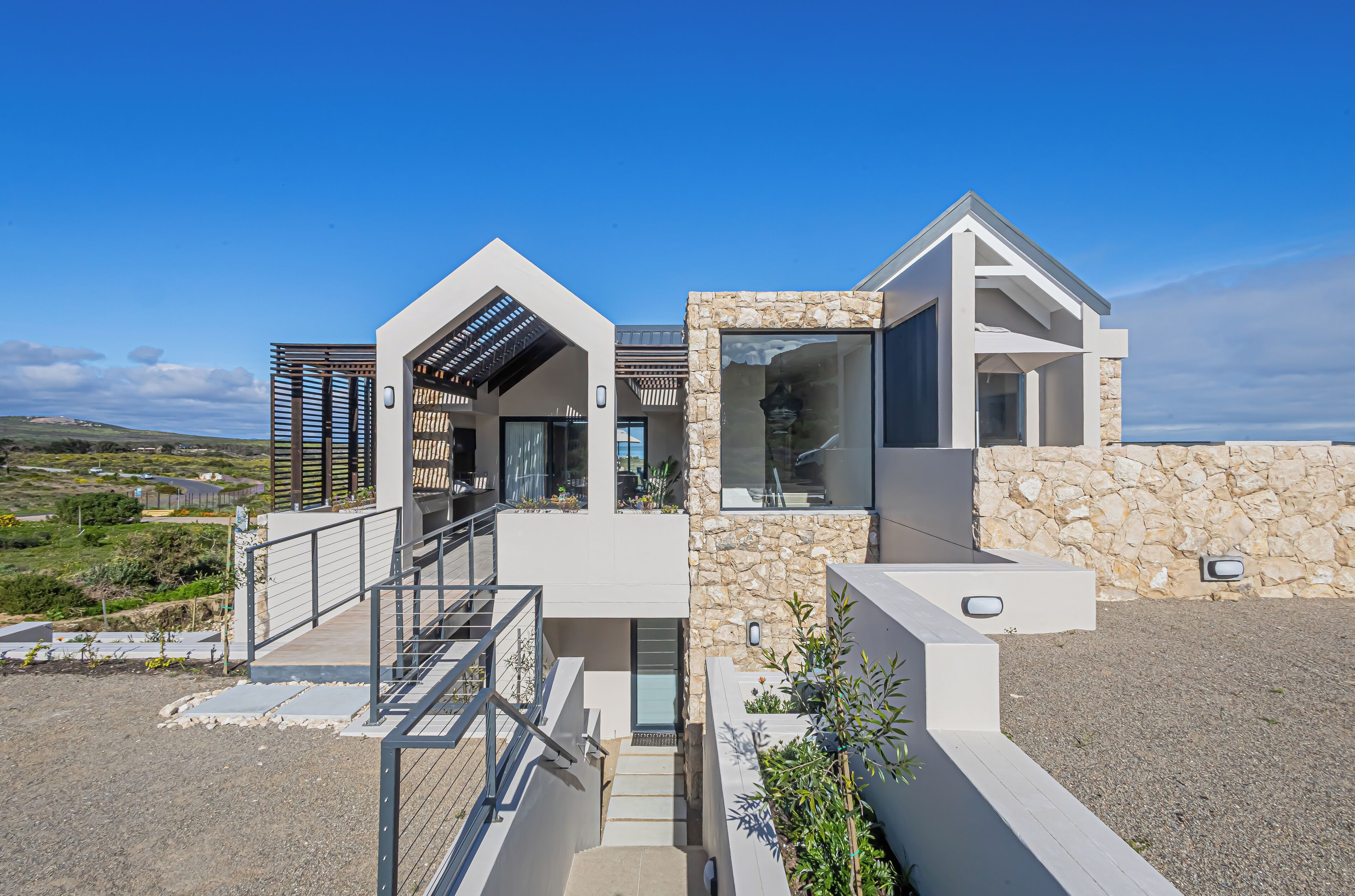 Une maison moderne avec une façade en pierre, une véranda en verre et un escalier en métal.
