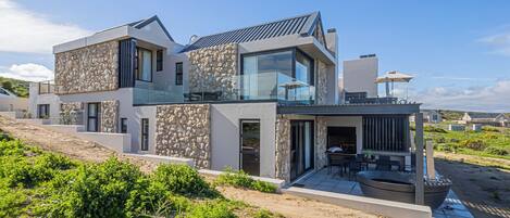 A modern house with a stone facade, large glass windows, and a patio with outdoor furniture.