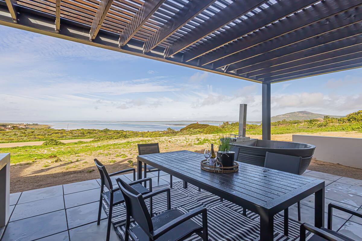 Un patio al aire libre con una mesa y sillas, con vistas a una playa y el océano.
