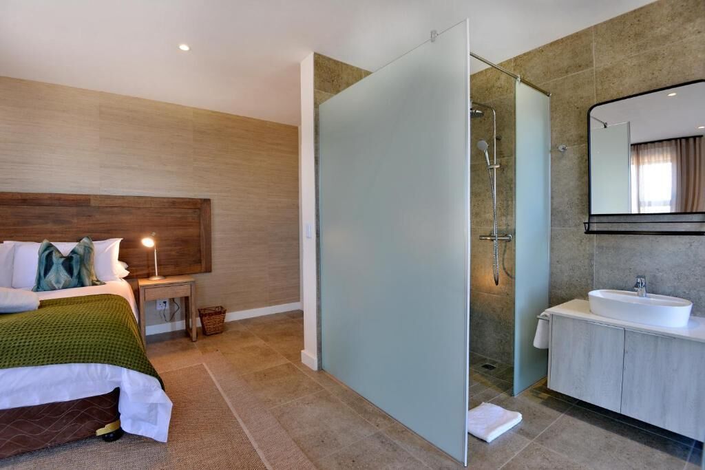 A modern hotel room with a bed, bedside table, lamp, and a glass shower enclosure.