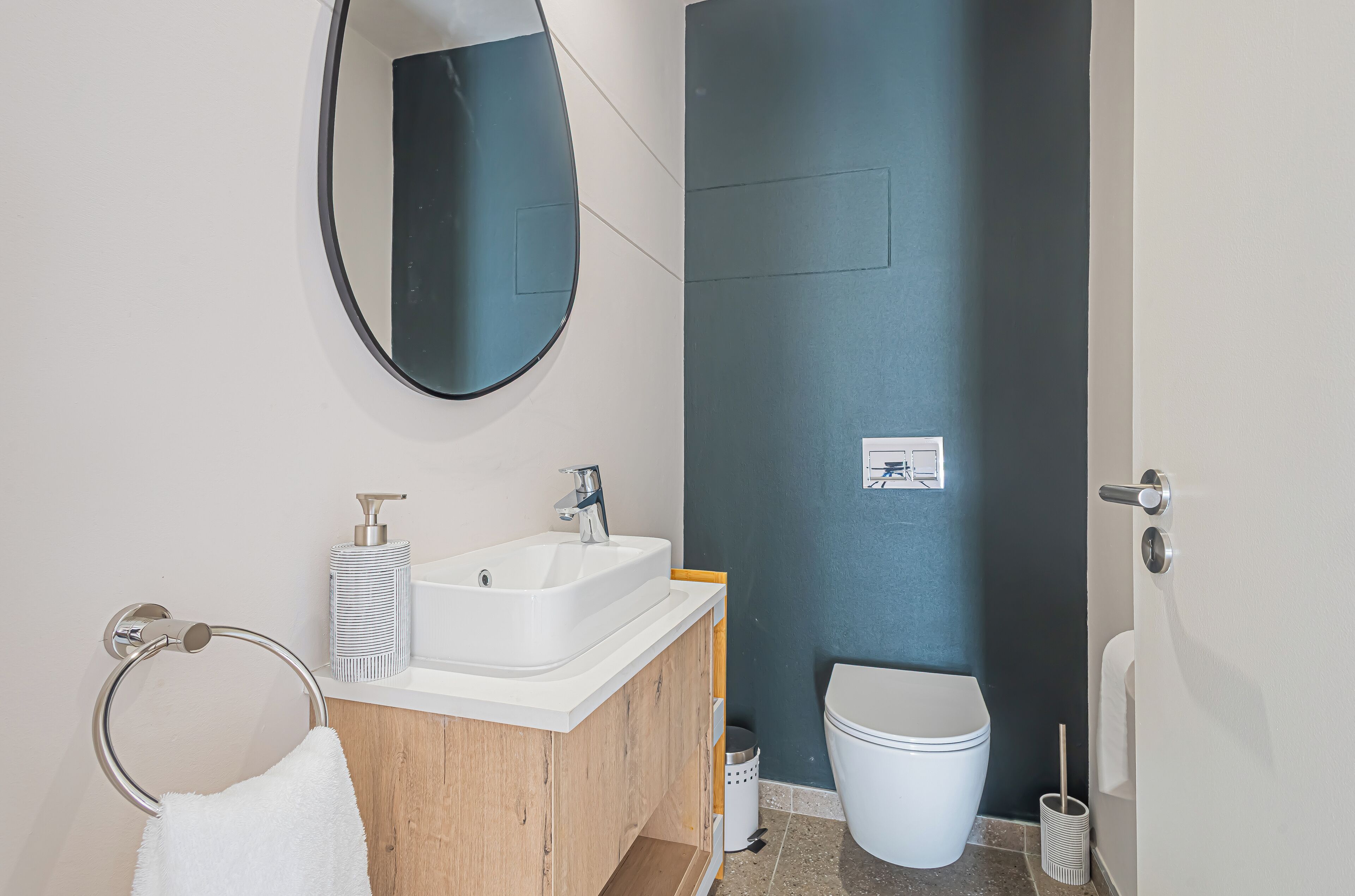Ein modernes Badezimmer mit einem Holzlagerfläschchen, einem weißen Waschbecken, einem Spiegel und einer Toilette.