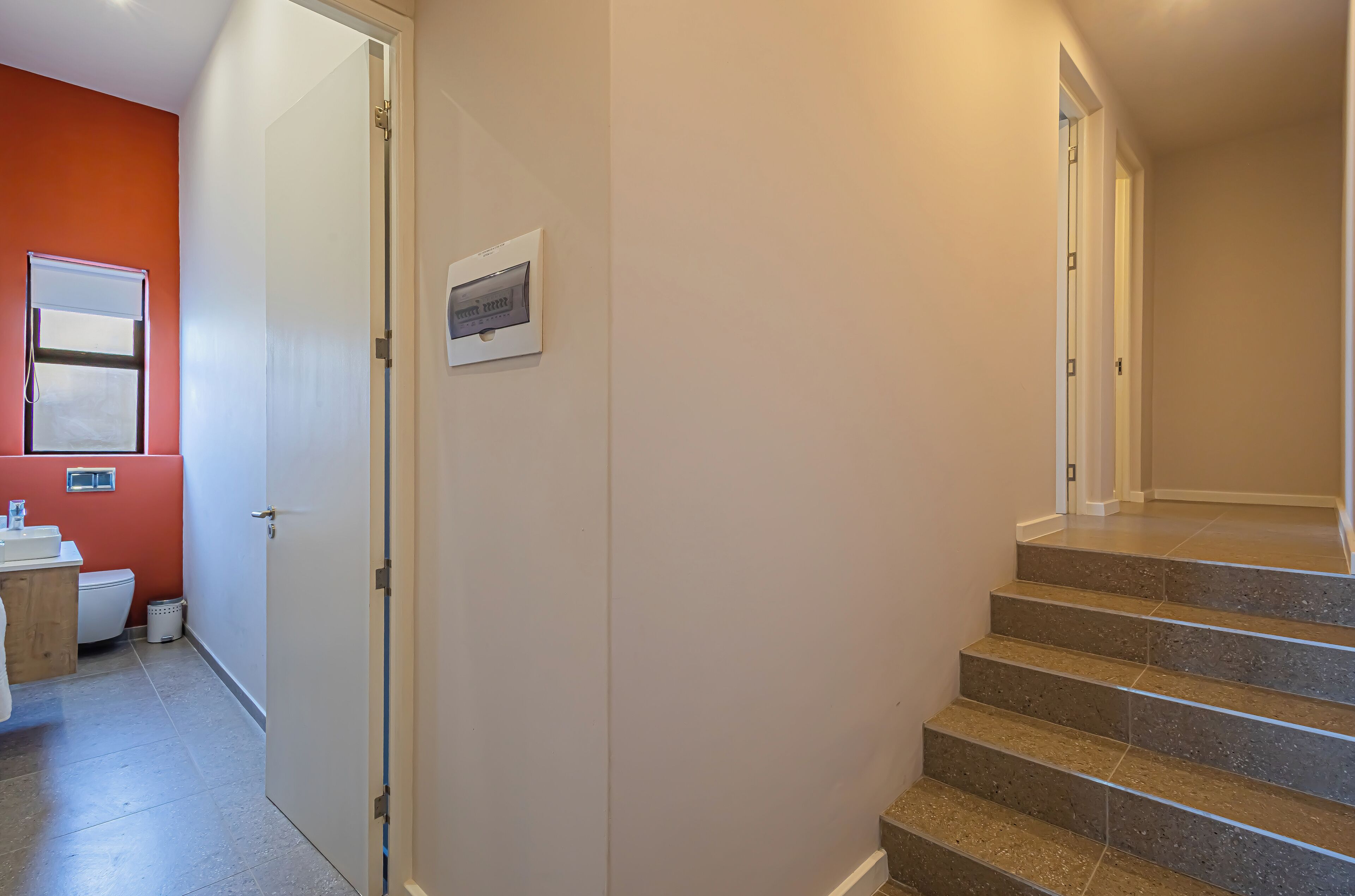 A hallway with a door leading to a bathroom, a staircase, and a small window.