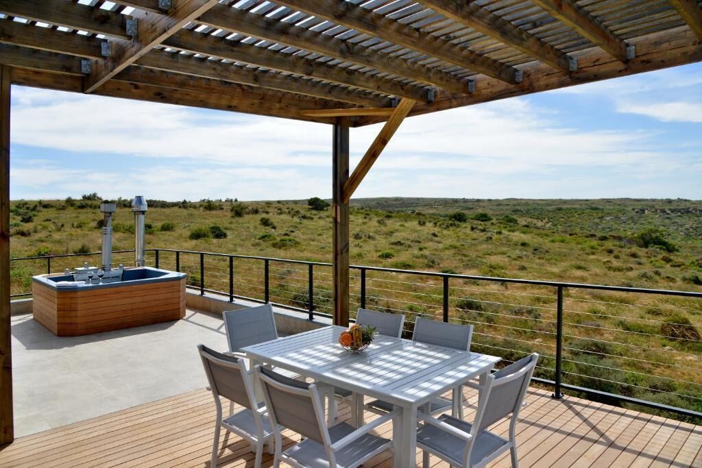 A covered outdoor deck with a table and chairs, a hot tub, and a view of a grassy landscape.