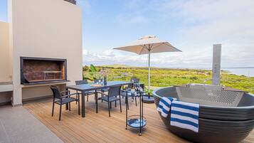 Une terrasse extérieure équipée d’un barbecue, d’une table à manger, de chaises et d’un jacuzzi.