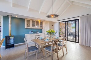 Comedor con mesa de madera dispuesta para cuatro, cocina integrada con pared de piedra y puerta corrediza de vidrio que da a un patio exterior.