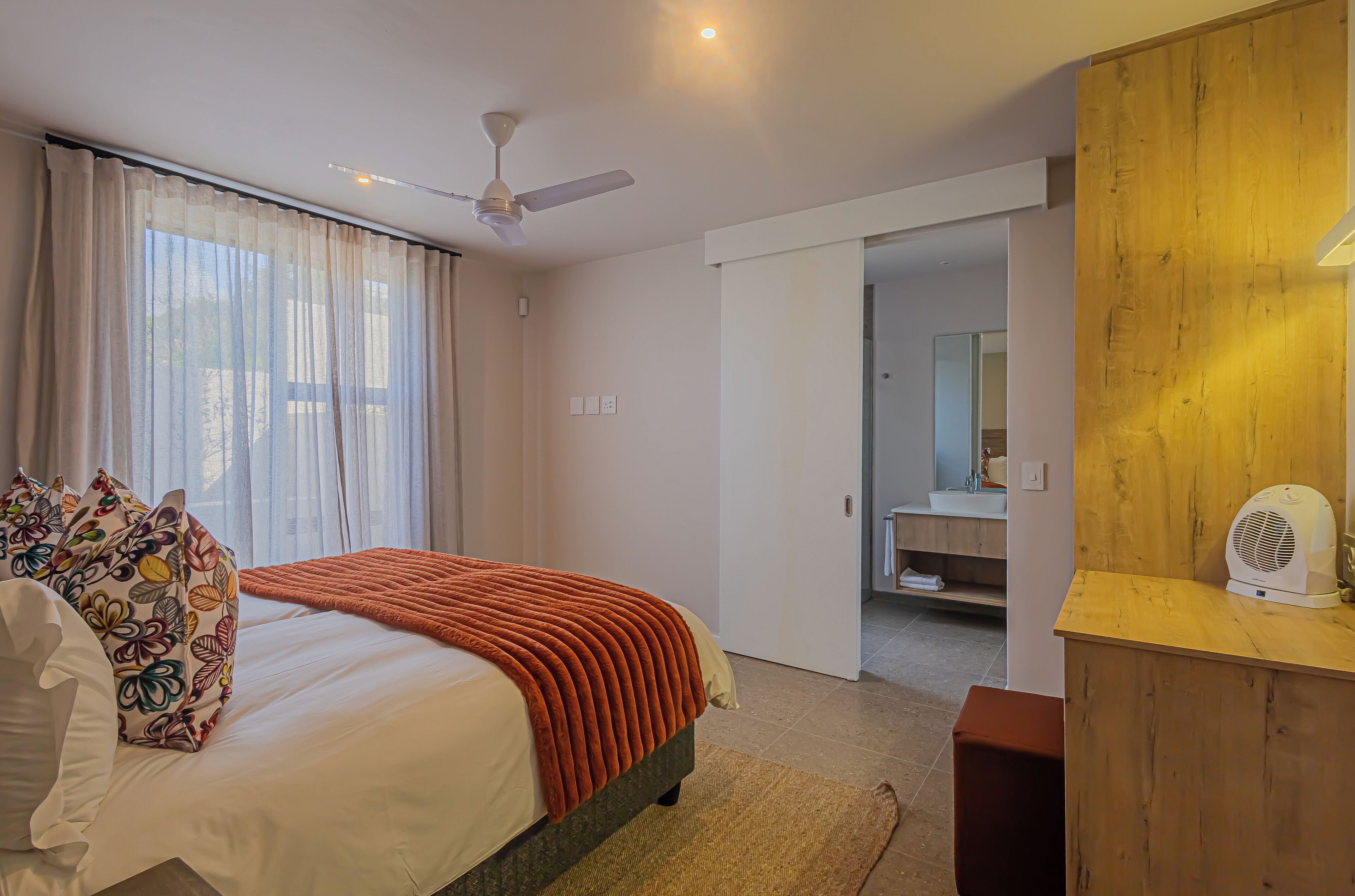 A hotel room with a bed, a ceiling fan, a wooden sideboard, and a bathroom visible through an open door.