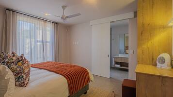 A hotel room with a bed, a ceiling fan, a wooden sideboard, and a bathroom visible through an open door.