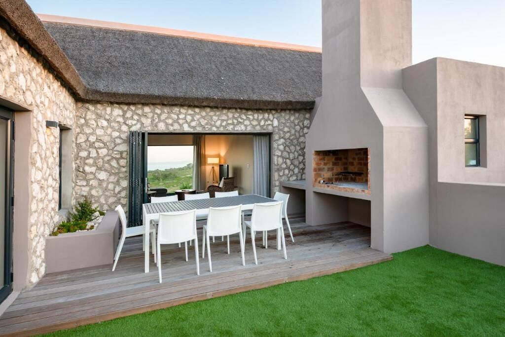A modern outdoor dining area with a stone wall, a thatched roof, and a built-in grill.