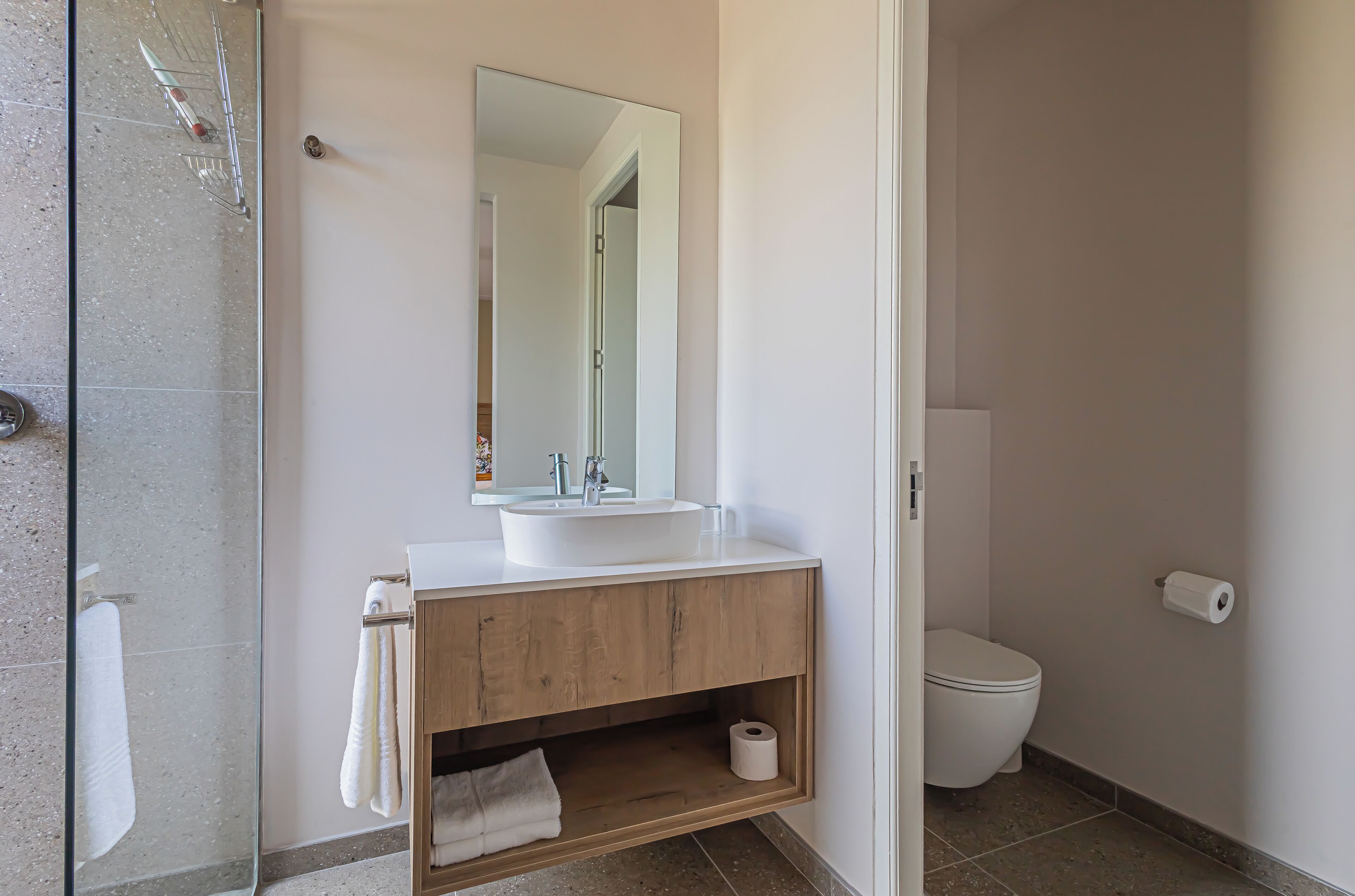 A modern bathroom with a glass shower enclosure, a wooden vanity with a sink, and a toilet.