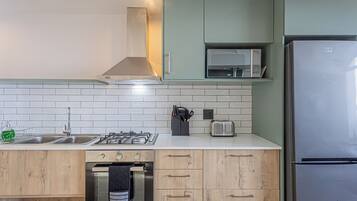 Une cuisine moderne équipée d’une cuisinière à gaz, d’un four à micro-ondes et d’un réfrigérateur en acier inoxydable.