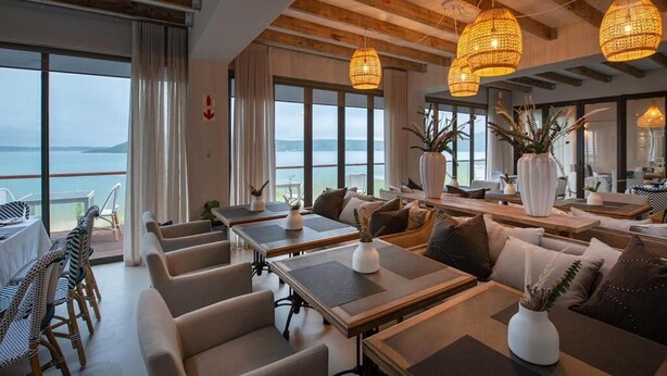 A modern dining area with tables and chairs, large windows with a view of the sea, and hanging wicker lamps. - The Shark Bay Private Villas (Langebaan)