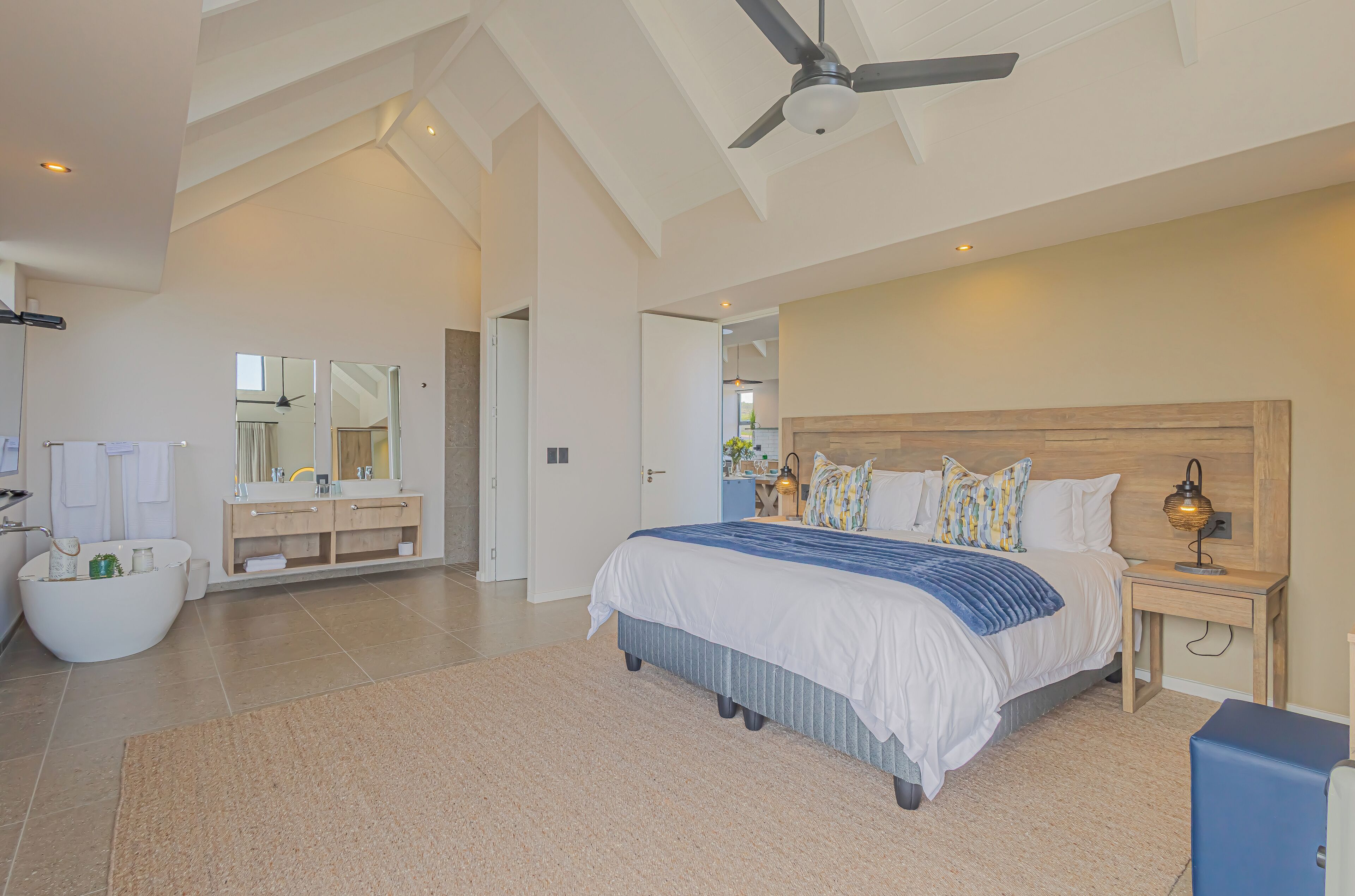 A spacious bedroom with a large bed, a ceiling fan, a wooden headboard, and a nightstand with a lamp.