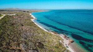An aerial view of a coastal area with a beach, clear blue waters, and sparse vegetation. - The Shark Bay Private Villas (Langebaan)