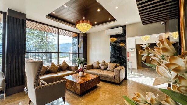 A spacious living area with a modern sofa set, a wooden coffee table, and a large chandelier. - The Orbit Regency (Gangtok)