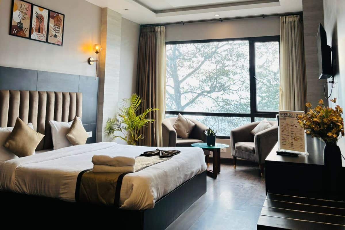 A modern hotel room with a large bed, a desk, a chair, and a window with a view of trees.