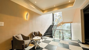 A hotel lobby with a checkered floor, two armchairs, a small round table, a staircase with glass railings, and a wall-mounted light fixture. - The Orbit Regency (Gangtok)