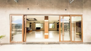 A modern building with large sliding glass doors leading to an interior with a central column, a sofa, and a dining area. - The Orbit Regency (Gangtok)