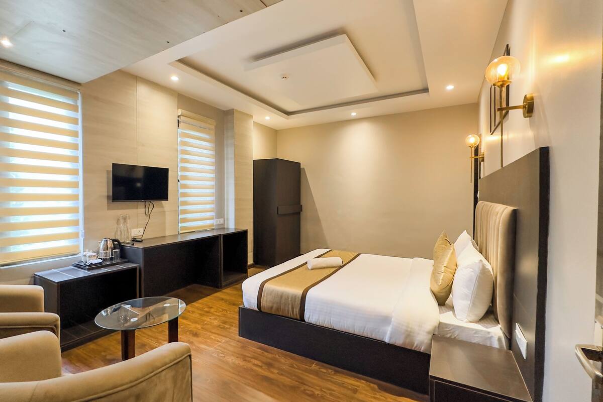 A modern hotel room with a large bed, a desk, a chair, and a TV mounted on the wall.