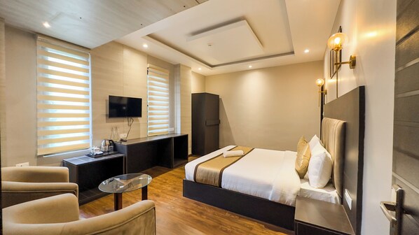 A modern hotel room with a large bed, a desk, a chair, and a TV mounted on the wall.