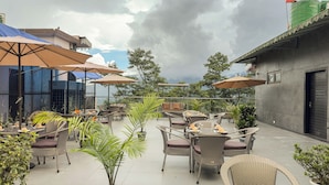 An outdoor patio area with wicker furniture, umbrellas, and potted plants. - The Orbit Regency (Gangtok)
