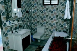 Un baño con pared de diseño de piedra, un lavamanos blanco, un inodoro y una bañera con cortina de ducha roja.