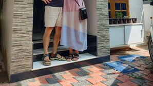 Un hombre y una mujer están de pie frente a la entrada de una casa de diseño moderno, con fachada de piedra y puerta de madera.